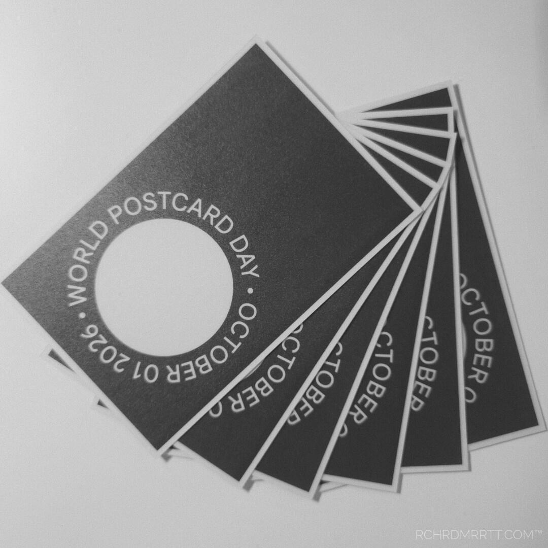 A square monochrome snapshot of a fanned-out stack of black-and-white World Postcard Day October 1st 2026 Postcards, in a minimalist style with a white border, designed and printed by Richard Merritt, from California USA.