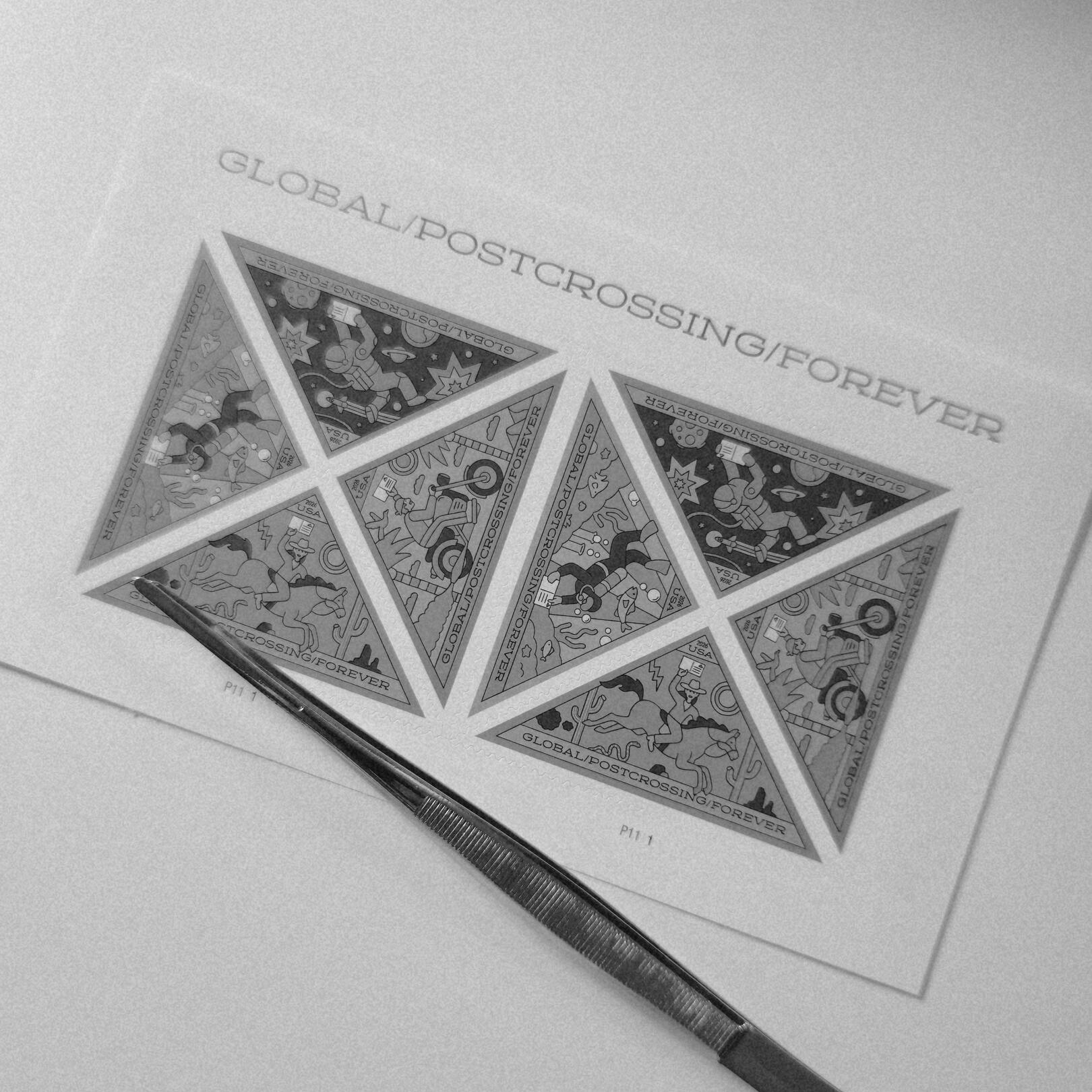 A close-up monochrome snapshot of the USPS Global Postcrossing Forever Stamp Sheet of eight triangular postage stamps and a pair of philatelic tongs laying across the stamp sheet.